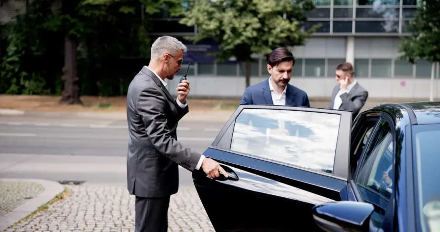 A professional chauffeur assisting a production crew member with equipment, showcasing our TV and film chauffeur service on a busy filming location
